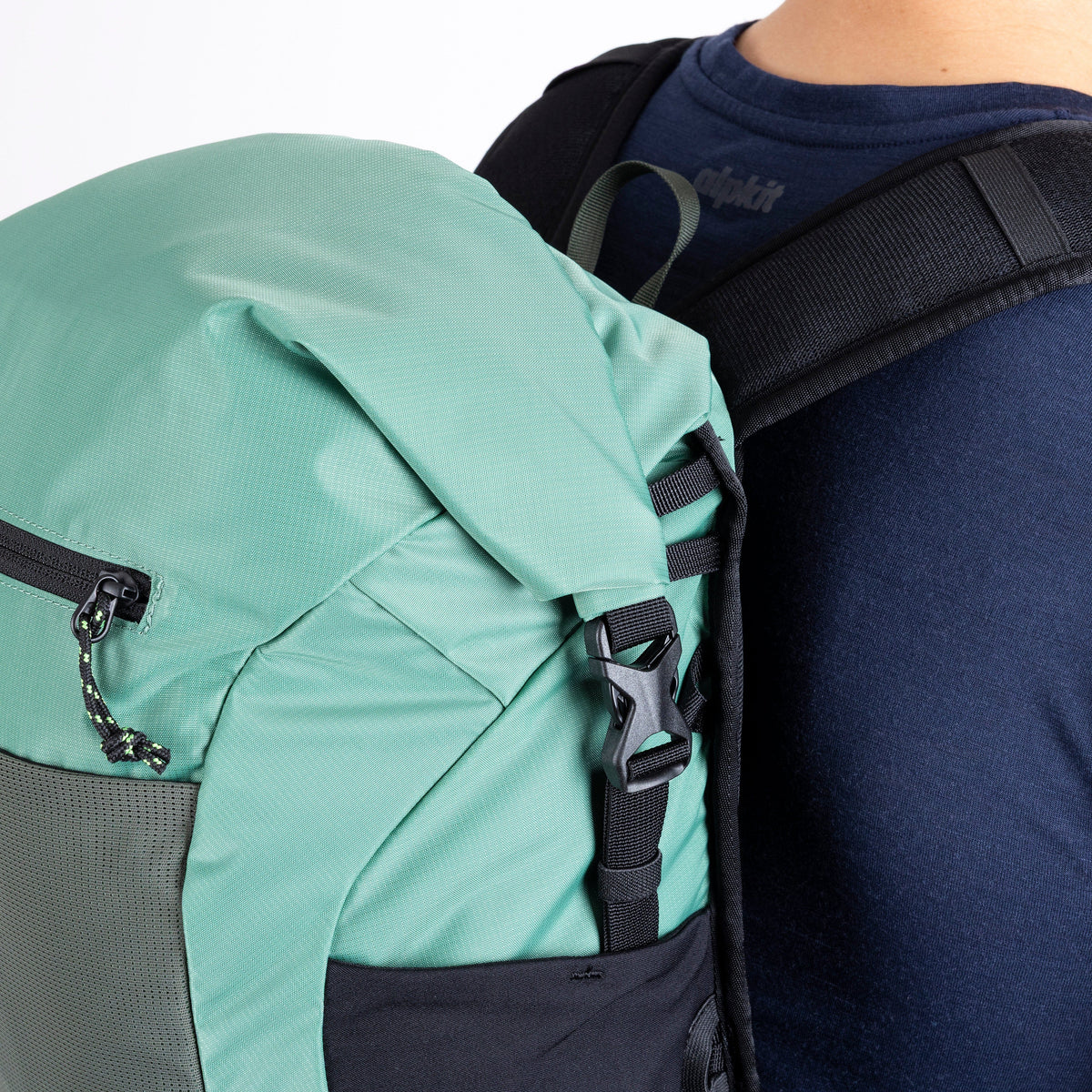 Green and gray backpack on a person's back with a focus on the straps and zippers.