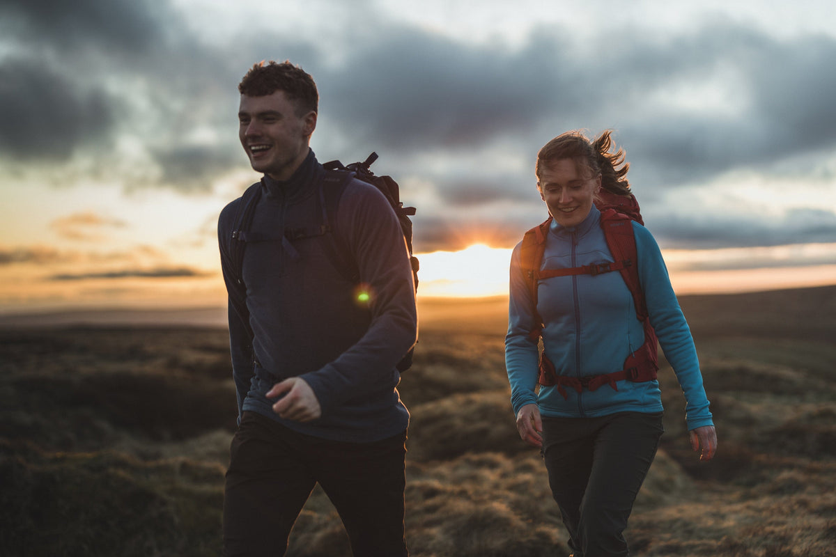 A man and a woman walking at sunset in the Peak District wearing a bright blue fleece jacket - action