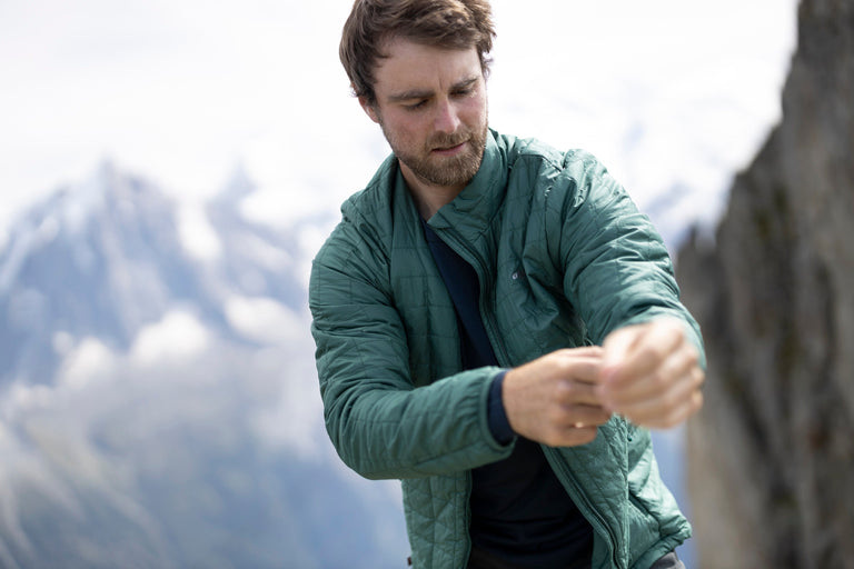 A man putting on a green PrimaLoft jacket in the French Alps - action - closed