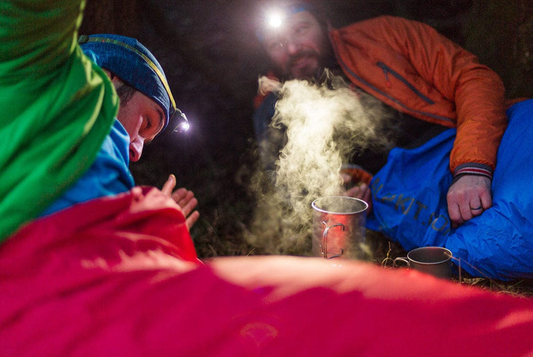 Two bikepackers having a chat before bed inside their bivvy bags - action - closed