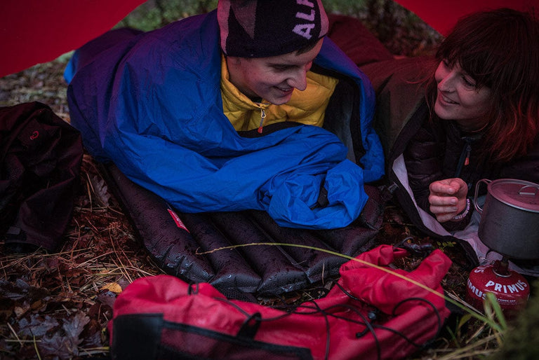 A man and a woman lying in their bivvy bags under a waterproof tarp - action