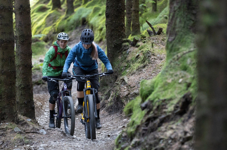 a man and a woman mountain biking through pine forest - action