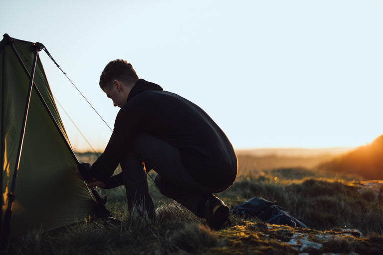 A man pitching a trekking pole tent at sunset in a black grid fleece - action - closed