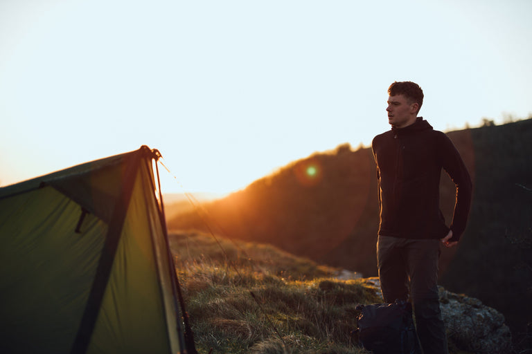 A man pitching a trekking pole tent at sunset in a black grid fleece - action