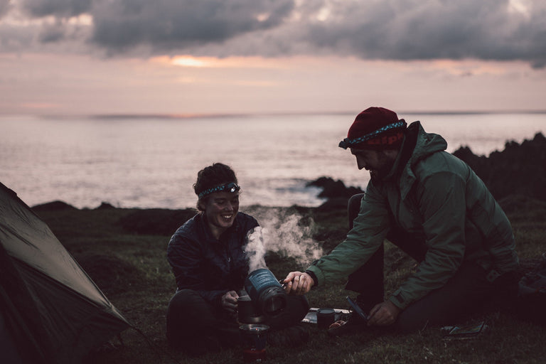 A man and woman cooking their tea on a camping stove in front of their tent at dusk  - action - closed