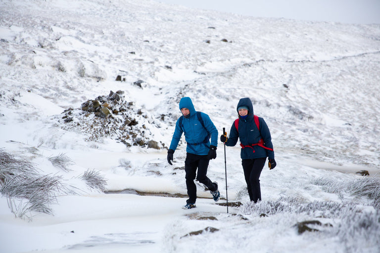 A man and a woman walking up a snowy bank on Kinder Scout in blue insulated jackets - action