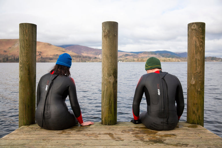 A man and woman sitting on the edge of a pier on Derwent Water in swimming wetsuits to get used to the temperature - action