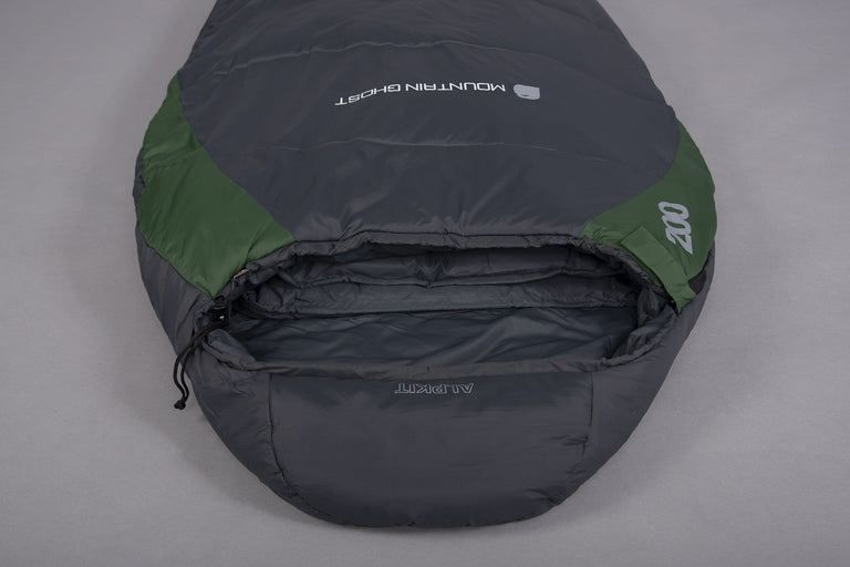 The hood of a Mountain Ghost 200 synthetic 2 season sleeping bag in green and grey laid on the floor upside down on a grey background