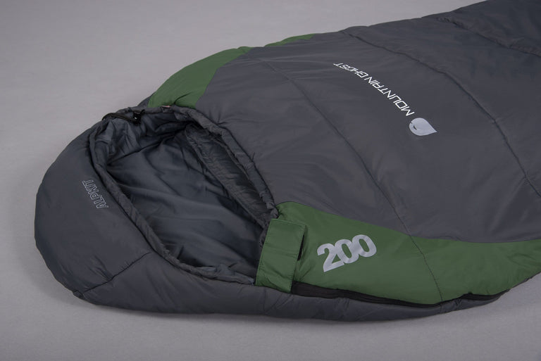 The hood of a Mountain Ghost 200 synthetic 2 season sleeping bag in green and grey laid on the floor on a grey background