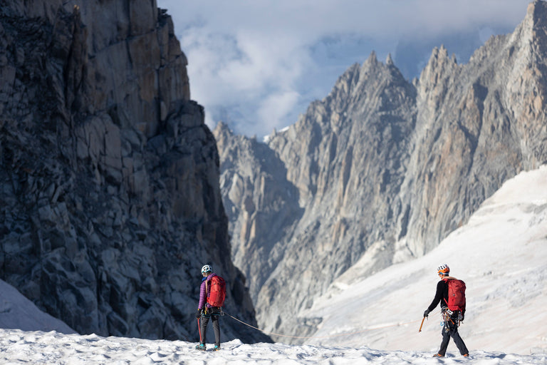 A woman walking across snow covered mountains in a purple down jacket 