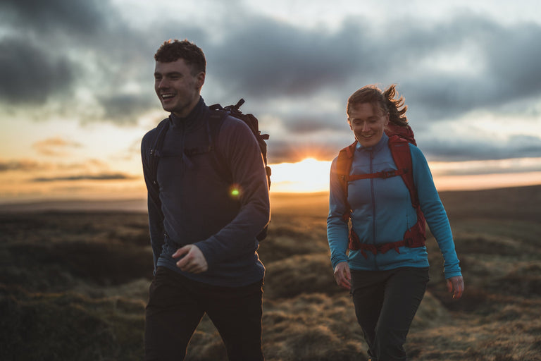 A man and a woman walking at sunset in the Peak District wearing a bright blue fleece jacket - action