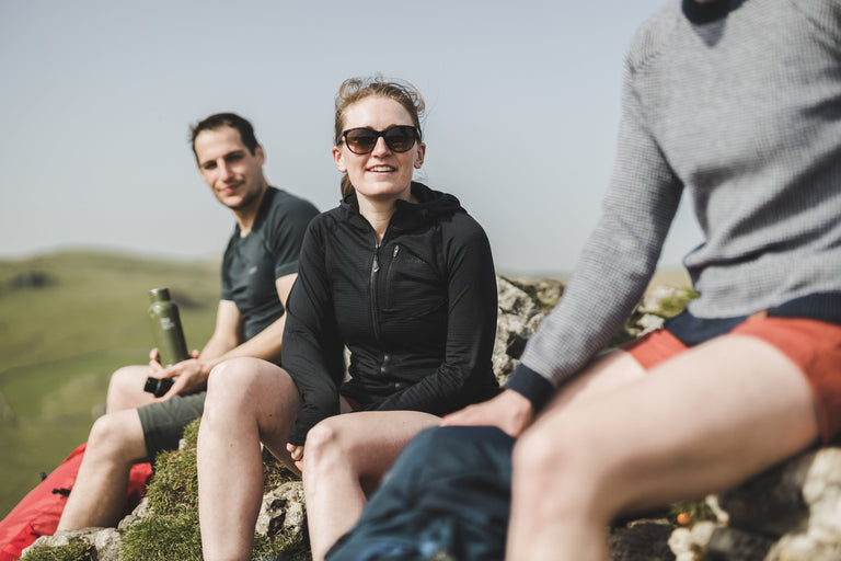 A woman sitting in a black lightweight fleece jacket on a hiking rest stop - action - closed